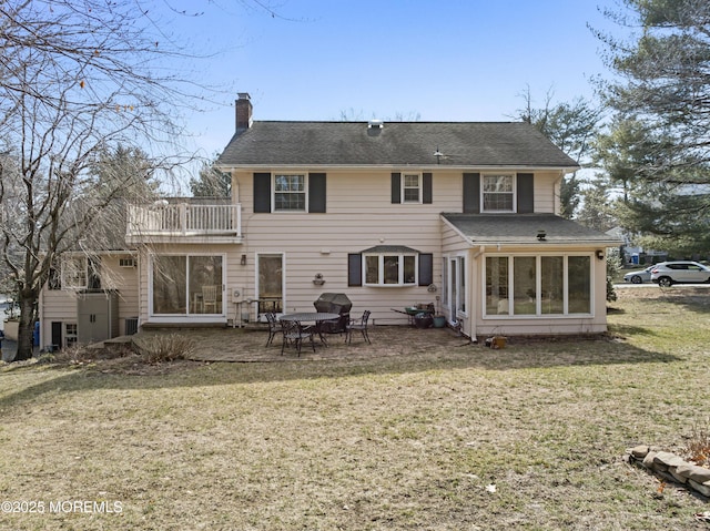 rear view of house featuring a balcony, a patio area, a chimney, and a lawn