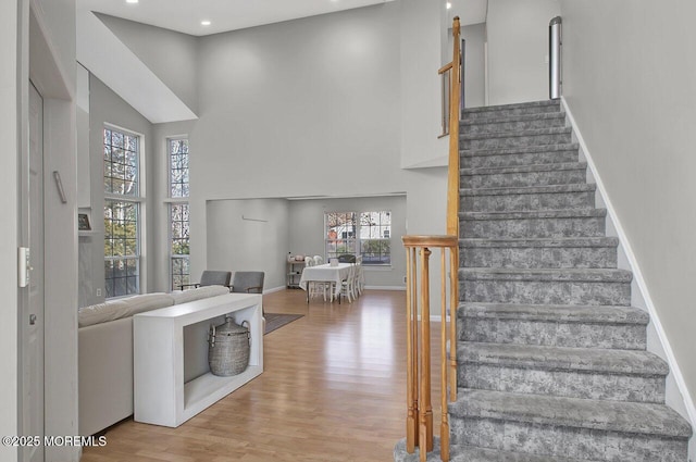 stairs featuring wood finished floors, a towering ceiling, and baseboards