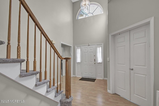 entrance foyer with baseboards, a towering ceiling, light wood-style flooring, stairway, and a chandelier