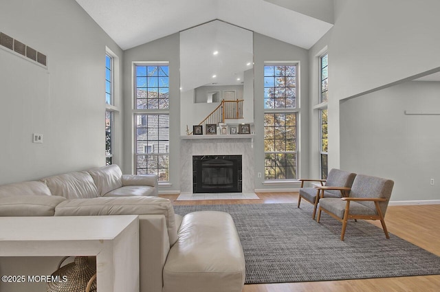 living area featuring a healthy amount of sunlight, a fireplace, high vaulted ceiling, and wood finished floors