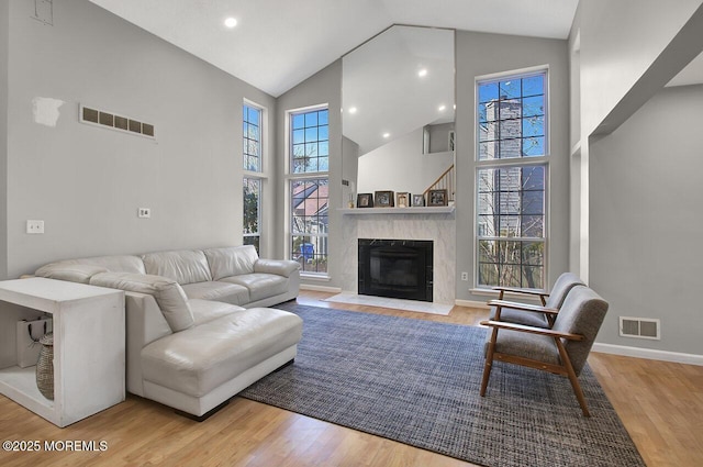 living room with high vaulted ceiling, a premium fireplace, visible vents, and wood finished floors