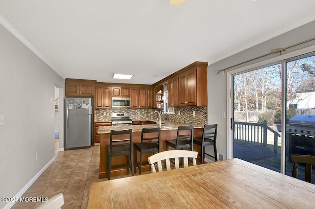 kitchen with appliances with stainless steel finishes, ornamental molding, backsplash, and a peninsula