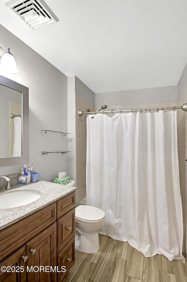 bathroom with visible vents, a shower with shower curtain, toilet, vanity, and wood finished floors