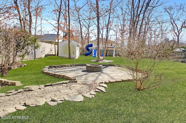 view of yard featuring an outdoor fire pit, a fenced backyard, an outdoor structure, a patio area, and a playground