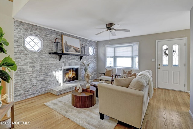 living area featuring a ceiling fan, a fireplace, brick wall, and wood finished floors