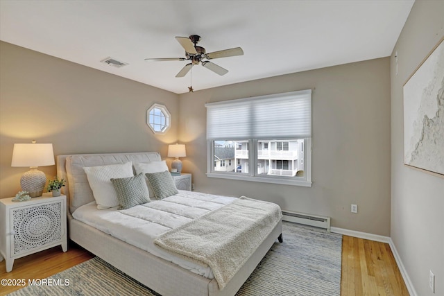 bedroom with baseboards, visible vents, a ceiling fan, wood finished floors, and a baseboard heating unit