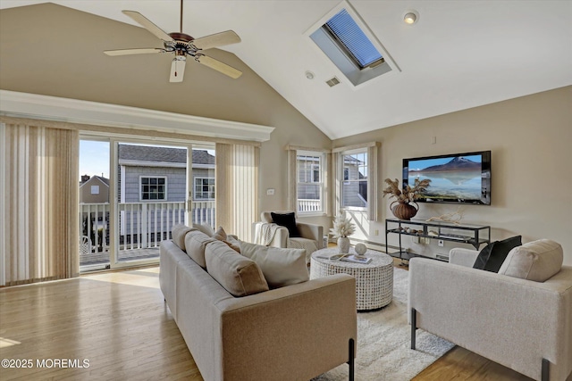 living room featuring light wood finished floors, a skylight, visible vents, ceiling fan, and high vaulted ceiling