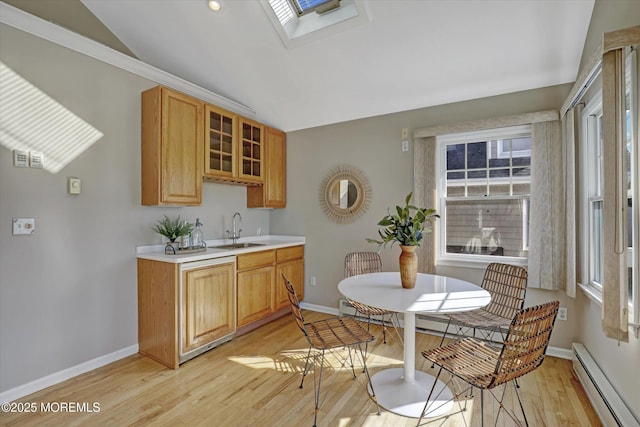 kitchen with vaulted ceiling with skylight, a sink, light countertops, baseboard heating, and light wood-type flooring