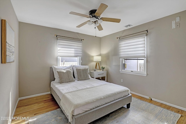 bedroom with a ceiling fan, visible vents, baseboards, and wood finished floors