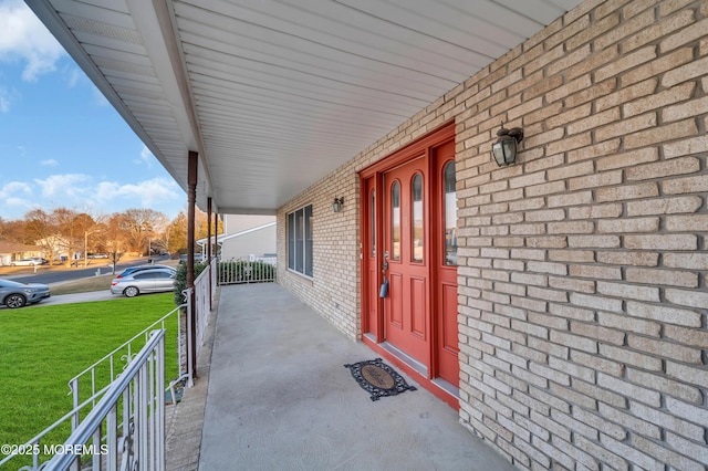 view of exterior entry featuring covered porch, a lawn, and brick siding