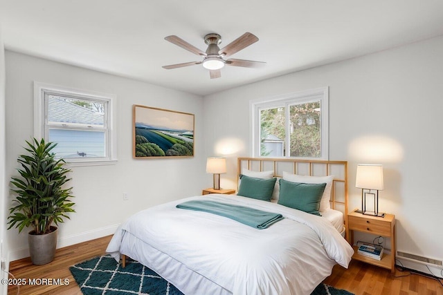 bedroom featuring multiple windows, a baseboard radiator, baseboards, and wood finished floors