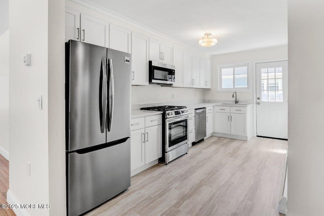 kitchen featuring light wood finished floors, light countertops, white cabinets, stainless steel appliances, and a sink