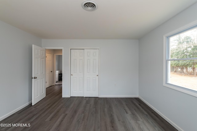 unfurnished bedroom with baseboards, visible vents, dark wood finished floors, and a closet