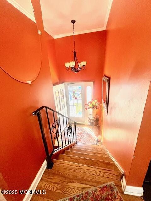 staircase with baseboards, a chandelier, crown molding, and wood finished floors