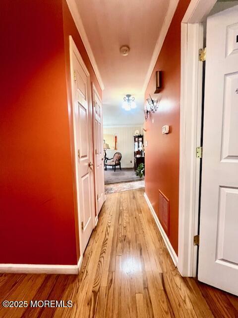 corridor with light wood-style floors, visible vents, and baseboards