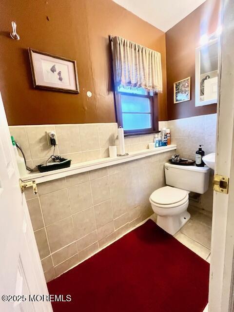 bathroom with toilet, tile walls, and tile patterned floors