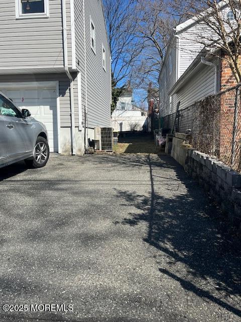 view of property exterior with a garage, driveway, and cooling unit