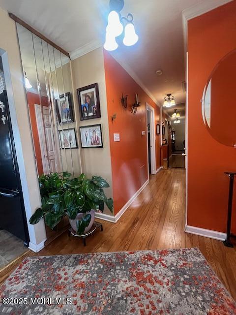 corridor with a notable chandelier, crown molding, baseboards, and wood finished floors