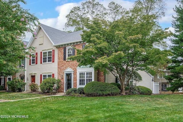 view of front of home featuring a shingled roof, a front lawn, and brick siding