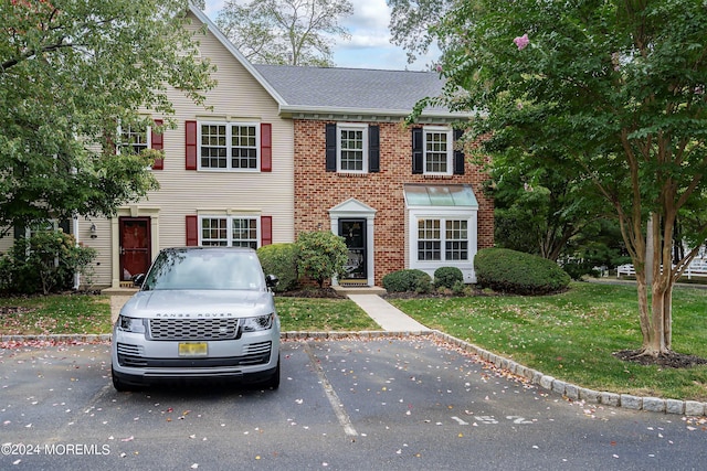 view of front of home with uncovered parking, brick siding, roof with shingles, and a front yard