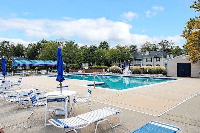 community pool with a patio, a storage unit, an outdoor structure, and fence