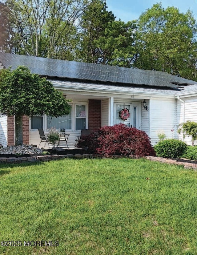 single story home featuring a front yard, covered porch, brick siding, and solar panels