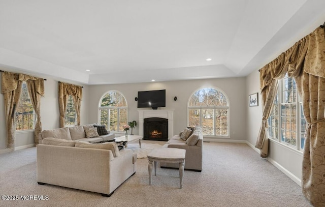 living area featuring a wealth of natural light, a lit fireplace, a tray ceiling, and baseboards