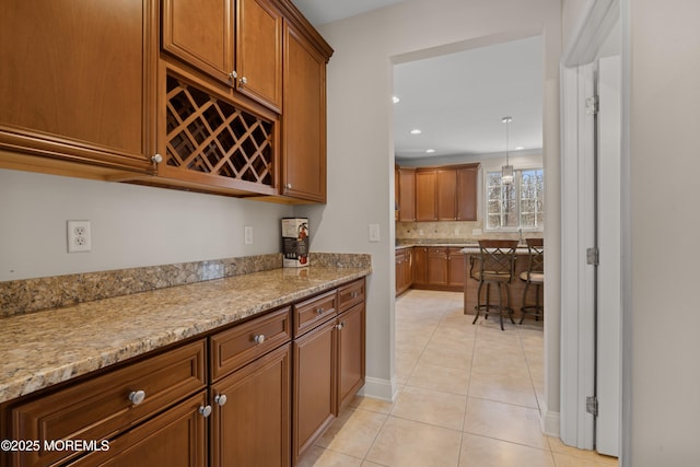 kitchen featuring brown cabinetry, light stone countertops, decorative backsplash, and light tile patterned floors