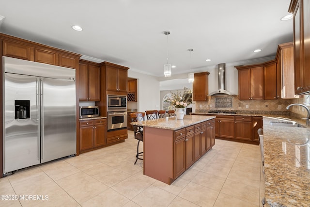 kitchen featuring light tile patterned floors, a center island, built in appliances, wall chimney range hood, and a sink