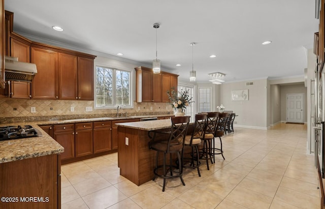 kitchen with tasteful backsplash, brown cabinetry, a kitchen island, range hood, and crown molding