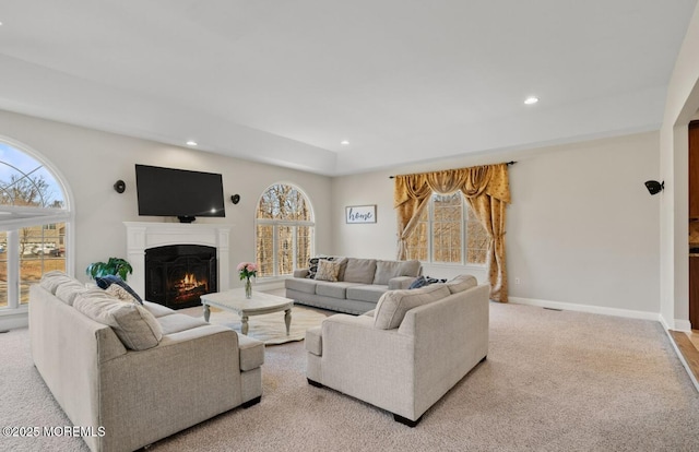 living area featuring a warm lit fireplace, recessed lighting, baseboards, and light colored carpet