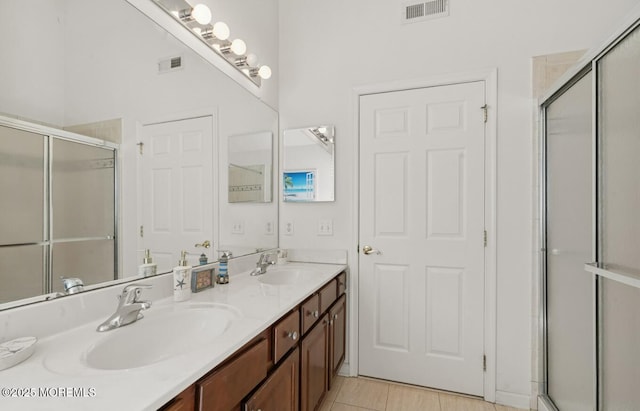 bathroom with a shower with shower door, visible vents, a sink, and double vanity