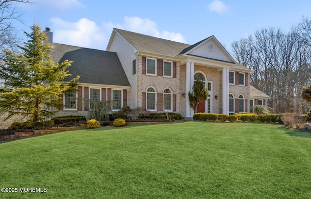 neoclassical / greek revival house featuring brick siding, a chimney, and a front lawn