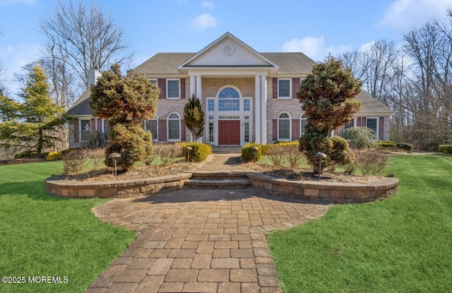 neoclassical / greek revival house featuring a front lawn and brick siding