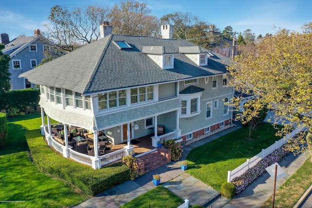 rear view of property featuring a shingled roof, a yard, a chimney, and a porch