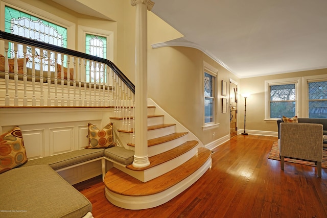 stairs with baseboards, wood-type flooring, crown molding, ornate columns, and a wealth of natural light