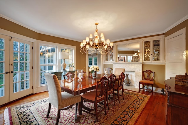 dining space with french doors, crown molding, a fireplace with flush hearth, wood finished floors, and a chandelier