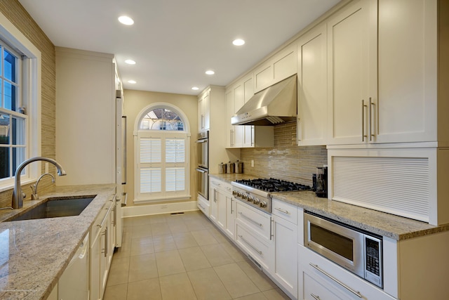 kitchen with light tile patterned floors, under cabinet range hood, a sink, appliances with stainless steel finishes, and tasteful backsplash