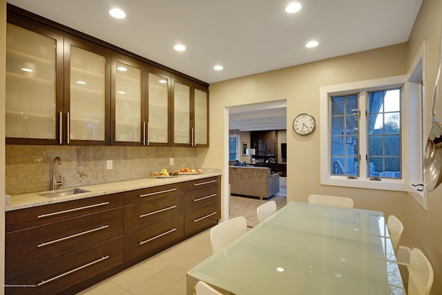 kitchen featuring tasteful backsplash, recessed lighting, glass insert cabinets, a sink, and dark brown cabinetry