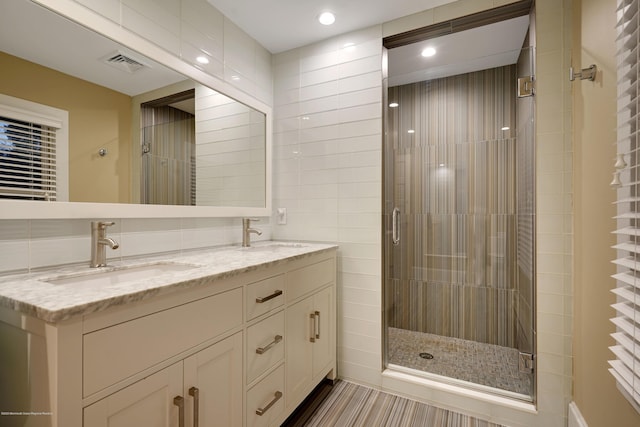 full bathroom with double vanity, a shower stall, visible vents, and a sink