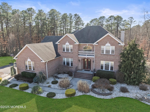 georgian-style home featuring brick siding, french doors, a chimney, and a balcony