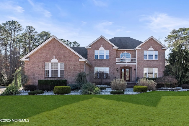 colonial home with a balcony, a shingled roof, a front lawn, and brick siding