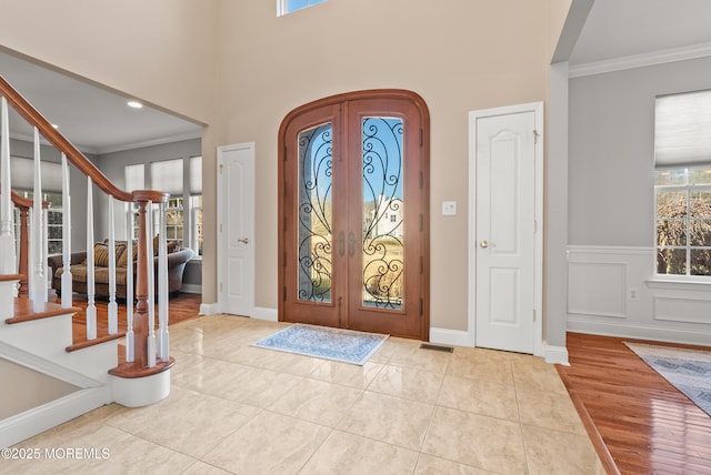 tiled entryway featuring arched walkways, french doors, crown molding, visible vents, and stairway