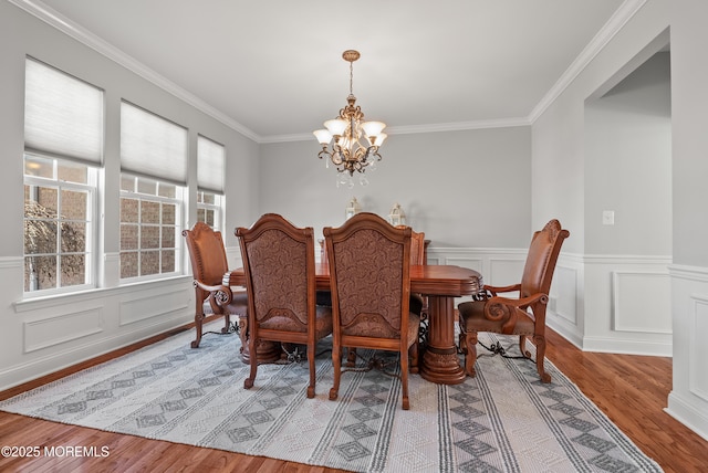 dining area featuring an inviting chandelier, ornamental molding, light wood finished floors, and wainscoting