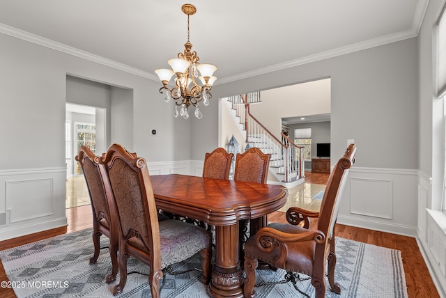 dining space featuring wood finished floors, ornamental molding, stairway, wainscoting, and an inviting chandelier