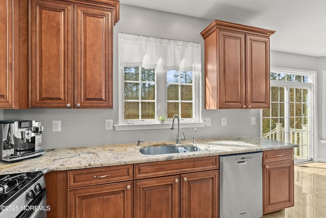 kitchen with stainless steel appliances, brown cabinetry, a sink, and light stone countertops