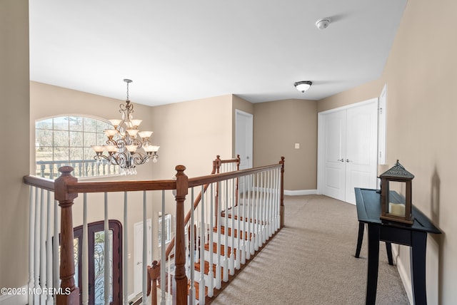 corridor featuring baseboards, carpet flooring, an upstairs landing, and an inviting chandelier