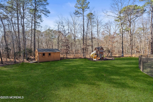 view of yard with a storage unit, a playground, a wooded view, and an outdoor structure