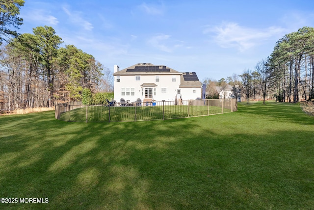 rear view of property with roof mounted solar panels, a fenced backyard, a yard, and a chimney