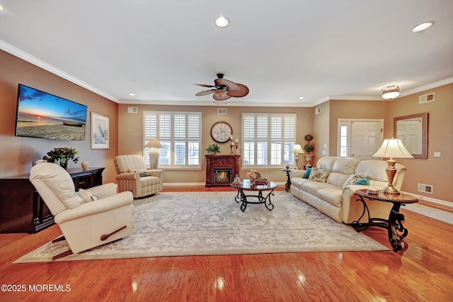 living room featuring ornamental molding, wood finished floors, a fireplace with flush hearth, and visible vents